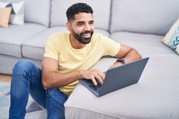 Wall Mural - Young arab man using laptop sitting on floor at home