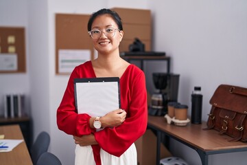 Wall Mural - Young chinese woman business worker smiling confident holding clipboard at office