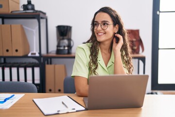 Sticker - Young hispanic woman working at the office wearing glasses looking away to side with smile on face, natural expression. laughing confident.