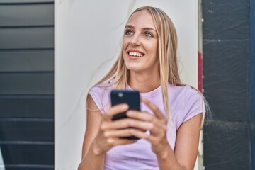 Sticker - Young blonde woman smiling confident using smartphone at street