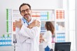 © Krakenimages.com - Middle age hispanic man working at pharmacy drugstore hugging oneself happy and positive, smiling confident. self love and self care