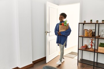 Wall Mural - African american woman holding groceries bag walking through the door at home