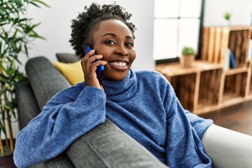 Poster - African american woman talking on the smartphone sitting on sofa at home