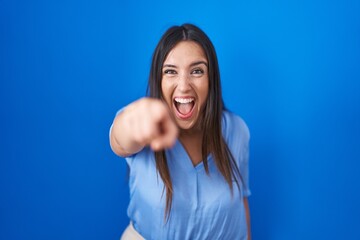 Wall Mural - Young brunette woman standing over blue background pointing displeased and frustrated to the camera, angry and furious with you