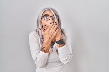 Wall Mural - Middle age woman with grey hair standing over white background shocked covering mouth with hands for mistake. secret concept.