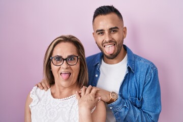 Canvas Print - Hispanic mother and son standing together sticking tongue out happy with funny expression.