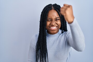 Canvas Print - African american woman standing over blue background angry and mad raising fist frustrated and furious while shouting with anger. rage and aggressive concept.