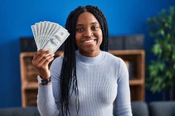 Poster - African american woman holding dollars banknotes looking positive and happy standing and smiling with a confident smile showing teeth