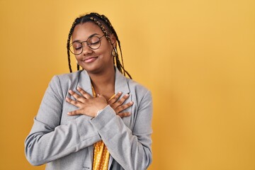 Wall Mural - African american woman with braids standing over yellow background smiling with hands on chest with closed eyes and grateful gesture on face. health concept.