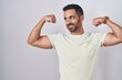 Hispanic man with beard standing over isolated background showing arms muscles smiling proud. fitness concept.