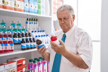 Poster - Middle age grey-haired man customer holding medication bottles at pharmacy