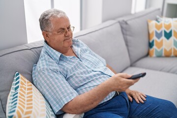 Sticker - Middle age grey-haired man watching television sitting on sofa at home