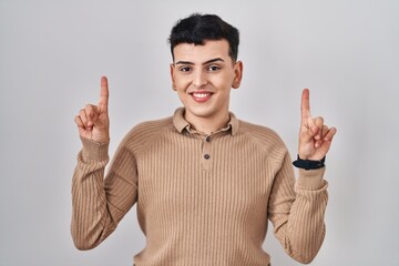 Sticker - Non binary person standing over isolated background smiling amazed and surprised and pointing up with fingers and raised arms.