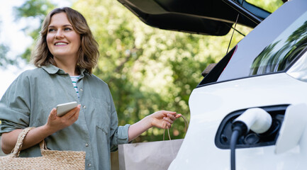 Sticker - Woman with shopping bag next to a charging electric car in the yard of a country house