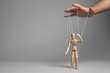 Man pulling strings of puppet on gray background, closeup. Space for text