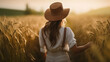 © Design Council - Portrait of a female farmer wearing overalls and a straw hat, standing in the middle of a green wheat field during sunrise Agriculture