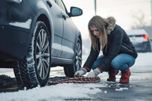 Woman putting on snow chains. Young woman putting snow chains on tires of her car. Road safety in winter conditions.