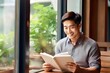 Asian man reading book in cafe, sitting near window, copyspace