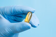 Doctor, pharmacist or scientist hand in blue glove holding omega 3 capsule. Vitamin pill or supplement on blue background. Healthcare and scientific research. Close up, selective focus