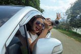 Fototapeta Tulipany - Smiling female driving vehicle on the road on a bright day. Sticking her head out the windshield