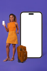 Wall Mural - Young cheerful attractive African American woman tourist with suitcase on wheels stands near phone with white screen and offers to use mobile apps to purchase air tickets posing in purple studio.