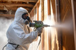 Man worker using plural component gun to spray polyurethane foam inside wooden frame house