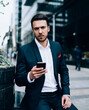 © BullRun - Serious businessman using smartphone on street
