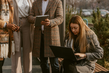 Wall Mural - Close up of blonde business woman typing on the laptop while her colleagues working on the tablet while standing next to her