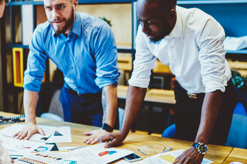 Wall Mural - Multiethnic coworkers standing at table with charts