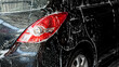 Soup foam covering on black car body and tail light. Self service car wash cleaning process. Car care concept