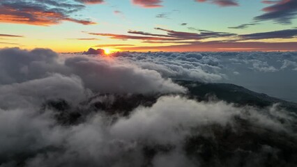 Wall Mural - Flying over dense clouds early in the morning. Aerial view of great sunrise above the clouds. Sun colors the cloud tops with warm orange light