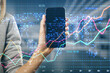 © Who is Danny - Close up of female hands holding cellphone with glowing forex chart on blurry office interior background. Crisis, and stock market fall concept. Double exposure.