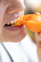 Sticker - Detailed shot of a woman bites yellow ripe tomato.