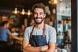 © Goffkein - Portrait of a handsome satisfied bearded young man with crossed arms and wearing apron working in a coffee shop
