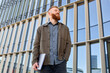 © makedonski2015 - A handsome red-haired freelancer man with a beard stands confidently against the backdrop of a city building and looks into the distance