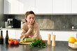 © Mix and Match Studio - Portrait of woman thinks what to cook with vegetables, looking at chopping board with tomatoes with thoughtful face, standing in kitchen preparing food