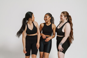 Wall Mural - Three joyful women in sportswear posing together isolated over white background