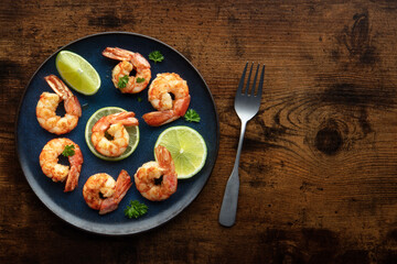 Wall Mural - Shrimps with lime, overhead flat lay shot, with copy space. Cooked shrimp on a blue plate, shot from the top on a rustic wooden background