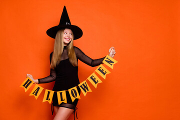 Canvas Print - Photo of attractive blonde teen woman look empty space hold garland dressed black halloween clothes isolated on orange color background