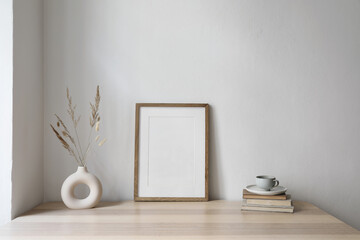 Wall Mural - Elegant neutral poster mockup. Wooden picture frame mockup on beige table. Modern boho vase with dry grass, old books. Cup of coffee. White wall background. Trendy Scandinavian interior, home office.