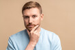 © DimaBerlin - Pensive puzzled thoughtful man looking at camera touching chin isolated on studio beige background. Embarrassed guy feeling confusion solves problems, struggling with choice. Male pondering idea.