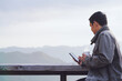 Traveler or tourist in coat drinks hot coffee and looks at a smartphone in the morning with mountain view in the background