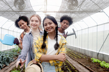 Wall Mural - Group of happy Multiethnic teenager friend work in vegetable farm, portrait of smiling young diverse farmer standing together, showing garden tools and watering can in agricultural field greenhouse.