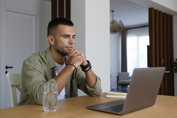 Bearded guy looking at the screen of his laptop. Adult education concept. Man taking an online course, watching a video lesson at home. Close up, copy space, interior background.