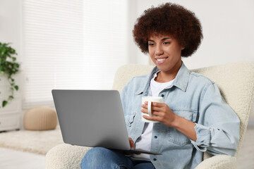 Wall Mural - Young woman using laptop and drinking coffee in room, space for text