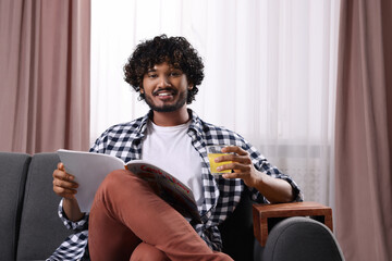 Sticker - Happy man holding glass of juice and magazine on sofa with wooden armrest table at home