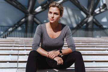 Wall Mural - Woman athlete wearing female sportswear sitting on bench of bleachers in outdoor stadium