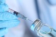 Doctor inserting syringe into glass vial with medication, closeup