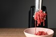 Electric meat grinder with beef mince on wooden table against grey background, closeup. Space for text