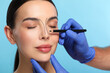 © New Africa - Woman preparing for cosmetic surgery, light blue background. Doctor drawing markings on her face, closeup
